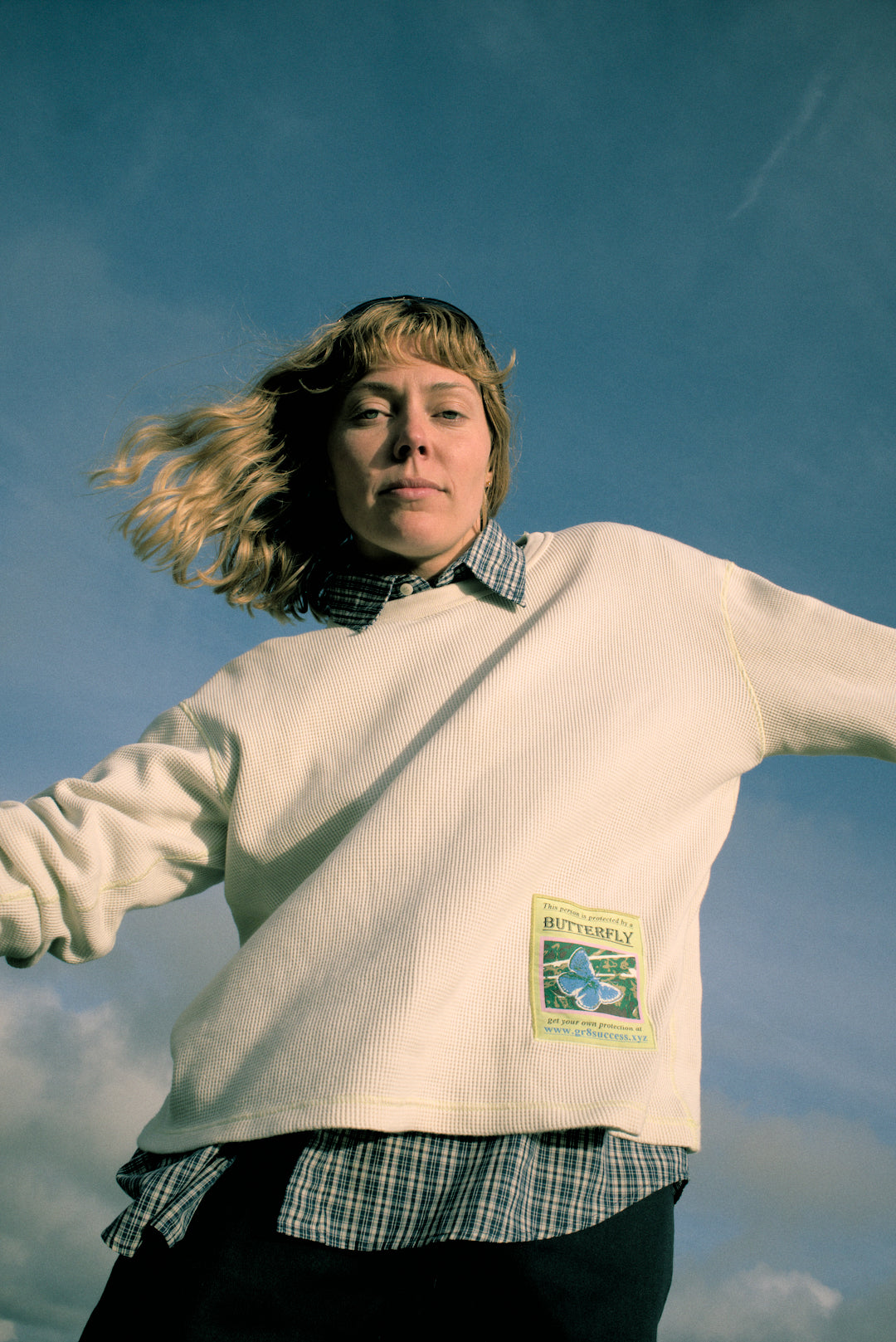 Person wearing a white sweater with a visible brand label against a blue sky.