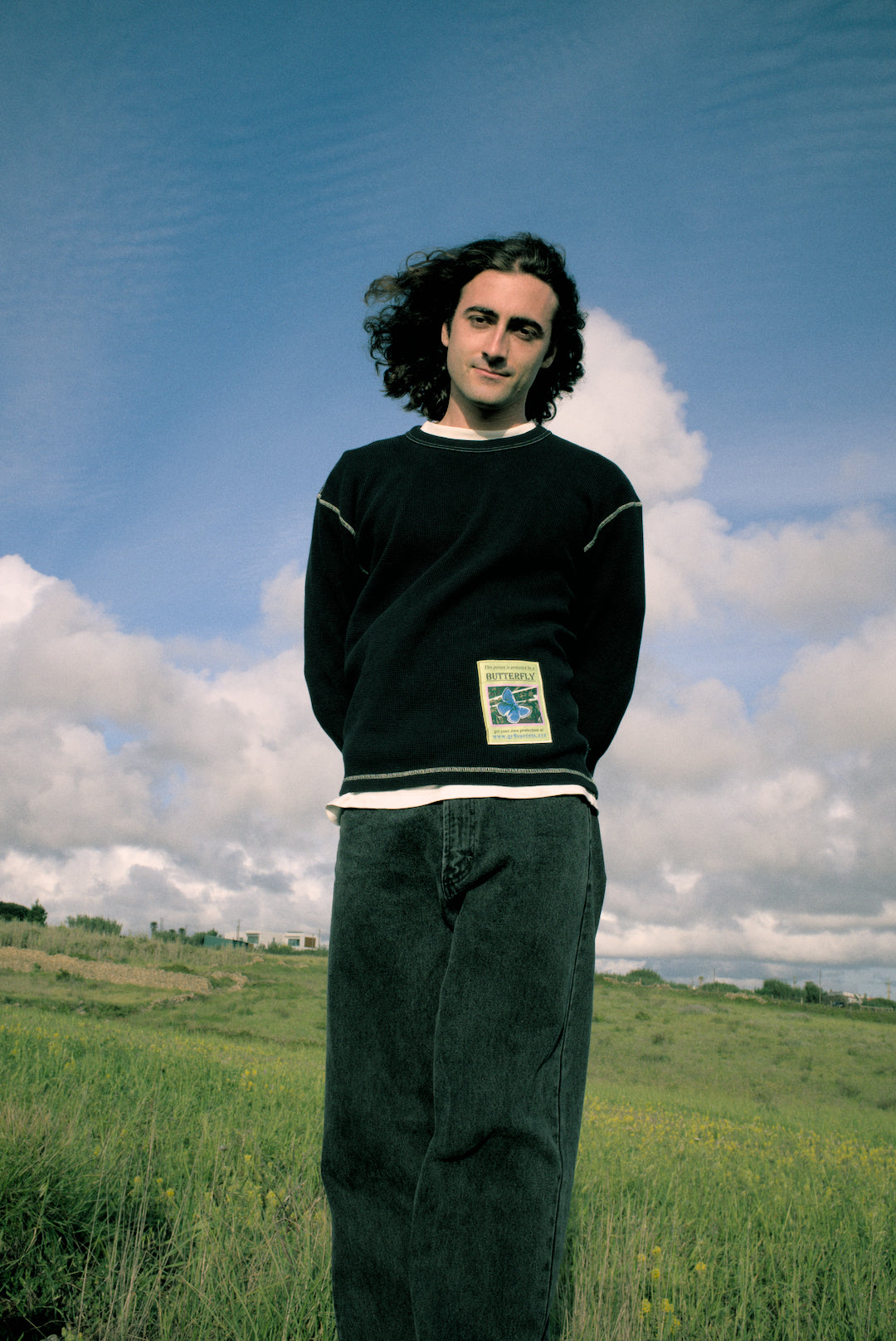 Person standing in a field with a blue sky and clouds in the background