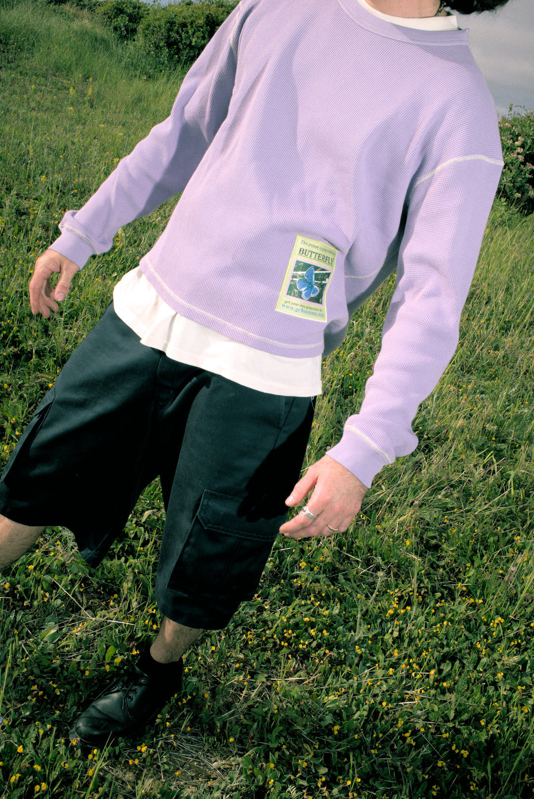 Person wearing a light purple sweatshirt with a green label in a grassy field. buzco gr8 success