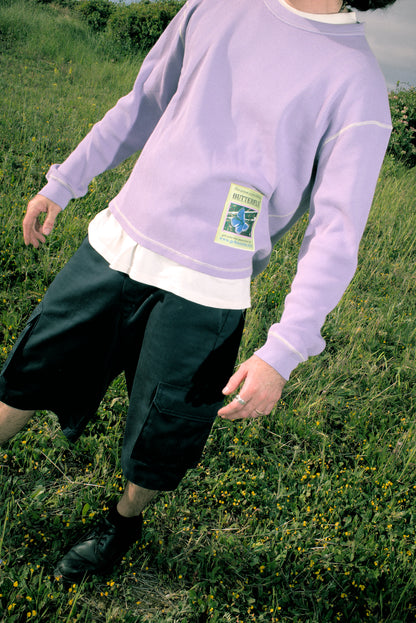 Person wearing a light purple sweatshirt with a green label in a grassy field. buzco gr8 success